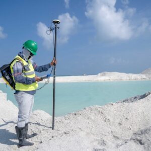 Surveyor in protective gear conducting measurements by a remote beach with GPS equipment.